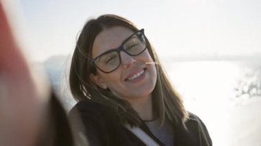 Gözlük takan mutlu kadın okyanus kenarında güneşin tadını çıkarıyor.