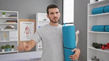 Öfkeli genç İspanyol adam rehabilitasyon kliniğinde reddedildiğini ifade ediyor yoga minderini tutuyor ve hoşlanmadığı için el sallıyor.