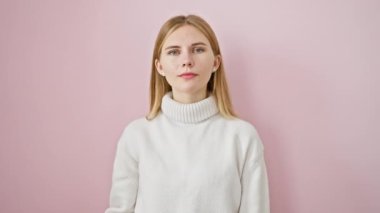 Neşeli, güzel sarışın kız. Başparmağıyla işaret veriyor, başarısını gösteriyor. Mutlu görünüyor, pembe arka planda tek başına duruyor.