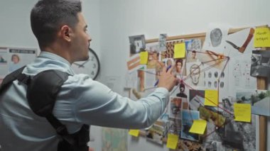 Odaklanmış genç bir İspanyol, karmaşık bir suç soruşturma kurulunu kanıt fotoğrafları ve notlarla analiz ediyor..