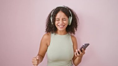 Genç, güzel İspanyol kadın müzik dinliyor ve pembe arka planda dans ediyor.