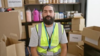 Bir depo dolusu bağış kutusunda güvenlik yeleği giymiş gülümseyen sakallı bir İspanyol 'un portresi..