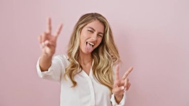 Gömlek giyen, ağzı açık gülümseyen, iki elini de gösteren genç sarışın kadın zafer işareti yapıyor. İki numara. izole edilmiş pembe arkaplan