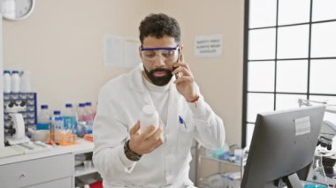 Laboratuvarda ilaç şişesini incelerken laboratuvar önlüklü İspanyol bilim adamı telefonla konuşuyor.