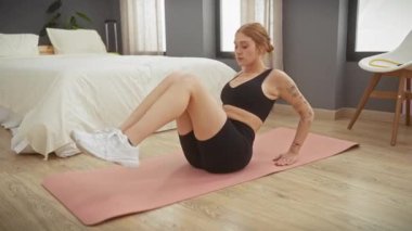 Genç bir kadın, minimalist mobilyalarla, mutluluk ve sükunet saçan temiz bir yatak odasında pembe bir paspasın üzerinde egzersiz yapıyor..