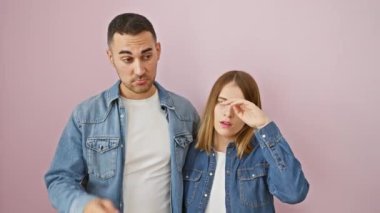 Kot giyen güzel bir çift, bir krizin stresiyle ayakta duruyorlar, elleri tedirgin pembe arka planda.