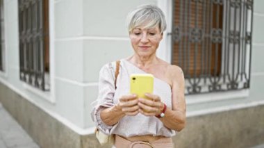 Şehir caddesinde akıllı telefon kullanan gri saçlı olgun bir kadın.