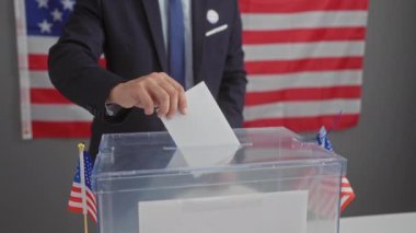 Takım elbiseli bir adam arka planda Amerikan bayrakları olan bir sandıkta oy veriyor. Amerika 'da demokrasiyi ve seçimleri simgeliyor..