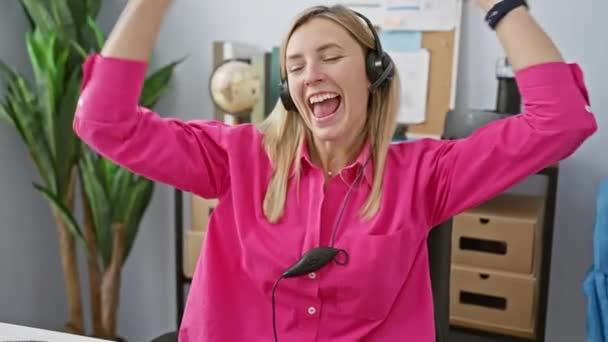 Веселая Молодая Женщина Розовой Рубашке Наслаждается Музыкой Наушниках Современном Офисе — стоковое видео
