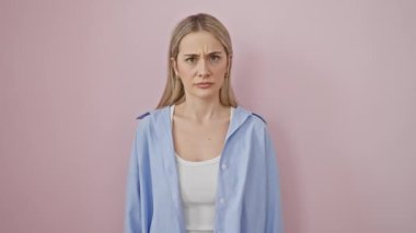 Gergin, genç, sarışın, şüpheci ve somurtkan bir kadın, soruna üzülüyor. Pembe gömlekli negatif düşünür, pembe arka planda izole edilmiş..