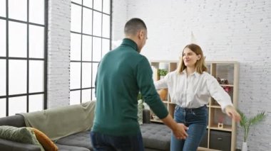 Parlak bir oturma odasında, şık bir dekorla kucaklaşan neşeli bir kadın ve erkek, evde sevgi ve arkadaşlığı iletir..