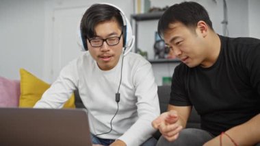 Sıcak bir oturma odasında dizüstü bilgisayarla uğraşan iki Asyalı, dostluk ve işbirliği gösteriyor..