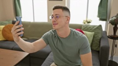 Genç İspanyol adam akıllı telefonuyla ev ortamında selfie çekiyor.