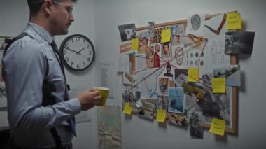 Yakışıklı İspanyol dedektif, elinde kahve fincanıyla karakoldaki kanıtları analiz ediyor..