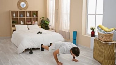 Genç bir adam iyi ışıklandırılmış çağdaş yatak odası ortamında esniyor, egzersiz yapıyor ve dinleniyor.