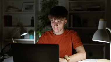 Genç bir adam gece geç saatlere kadar evinde çalışıyor. Masasında lamba olan karanlık bir odada dizüstü bilgisayar kullanıyor..