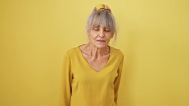 Tüh! Gri at kuyruklu orta yaşlı bir kadın unutulmuş bir hata yüzünden kafasına tokat attı. hafıza hatası konsepti onu sarı arkaplanda izole ediyor.