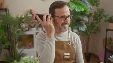 Gülümseyen sakallı adam çiçekçi dükkanında sesli mesaj dinliyor..