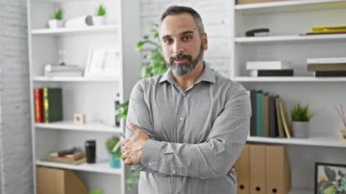 Gri saçlı, kendine güvenen, sakallı, gömlek giyen, modern beyaz ofis içinde kollarını kavuşturan olgun bir adam..