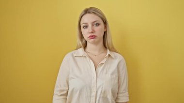 Güzel sarışın kadın, yorgun ve sıkılmış görünüyor, depresyon sorunlarını düşünüyor. Gömlek giyiyor, kollarını kavuşturup üzgün duruyor, sarı arka planda soyutlanmış..