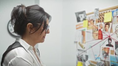 Odaklanmış bir kadın dedektiflik bürosundaki bir mantar panoda kanıtları analiz eder..