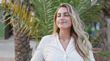 Kendine güvenen genç sarışın kadın, doğanın tadını çıkarıyor, güzel yeşil bir parkta neşeyle gülüyor ve gülümsüyor..