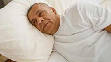 Düşünceli, orta yaşlı, İspanyol bir adam yatakta, evde, düşünceli bir ifadeyle yatıyor..