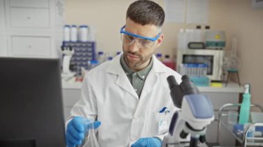 Odaklanmış bir adam yeşil bir sıvıyı incelerken koruyucu gözlük ve eldiven takarak laboratuvarda deneyler yapar..