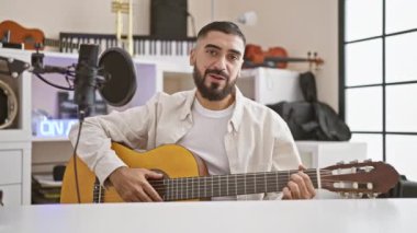 Gülümseyen sakallı adam modern bir müzik stüdyosunda gitar çalıyor. Yetenek ve yaratıcılığı kapalı mekanda sergiliyor..