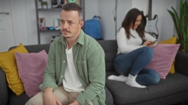 Endişeli adam oturuyor, kadın oturma odasında akıllı telefon kullanıyor..