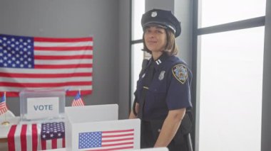 Gülümseyen bir kadın polis, Amerikan bayraklarıyla süslenmiş bir seçim merkezinde baş parmağını kaldırıyor..