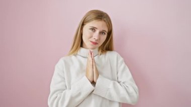 Kendine güveni tam sarışın bir kız, elleri pembe izole edilmiş arka planda coşkuyla dua ediyor, acıkıp tatlı bir af dilerken gülümsüyor..