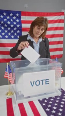Kendine güvenen bir kadın, arka planda Amerikan bayraklarıyla Amerikan seçim merkezinde oy veriyor. Demokrasiyi ve vatandaşlık görevini simgeliyor..