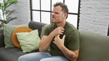 Evde, genç, kızgın adam, öfkeyle bağırarak, öfkeyle, öfkeyle, kollarını kaldırarak, kanepeden dışarı salıyor.