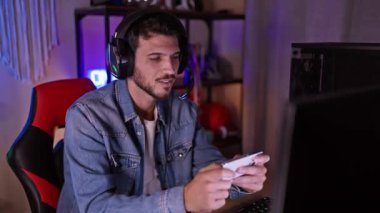 Kulaklıklı bir adam geceleri rahat, renkli bir odada oyun oynuyor. Teknoloji ve eğlence sergiliyor..