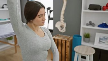 Fizyoterapi kliniğinde egzersiz ekipmanları ve anatomi modelleriyle gerinen odaklanmış bir kadın..