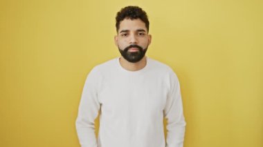 Neşeli genç adam zafer işareti çakıyor, özgüvenle gülümsüyor, sarı izole arkaplanda duruyor, kameraya bakıyor..