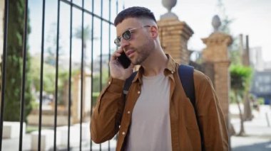Güneşli bir şehir sokağında, sakallı şık bir İspanyol adam cep telefonuyla konuşuyor, rahat ve havalı bir hava yayıyor..