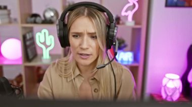 Kendine güveni tam genç sarışın kadın flamalı. Geceleri rahat odasında oyun oynarken mikrofona canlı bir şekilde gülümsüyor ve konuşuyor.