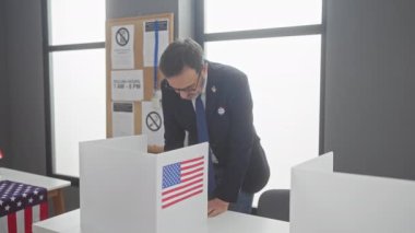 Takım elbiseli olgun bir adam, bayrakları ve mahremiyet kabinleriyle bir Amerikan oy kullanma merkezinde oy veriyor..