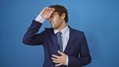 İş elbisesi giymiş hasta genç adam grip ve ateşle savaşıyor, acı içinde yüzükoyun yatıyor, el ele, virüsten etkilenmiş, mavi arka planda izole edilmiş.