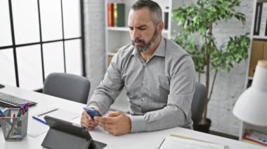 Ofisinde gri sakallı, akıllı telefondan bıkmış, teknolojik sorunlar tasvir eden sinirli, olgun bir adam..