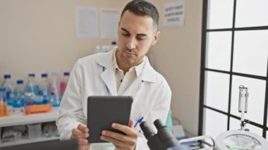 Laboratuvar önlüklü bir adam ve kadın modern bir laboratuvar ortamında bir tabletteki verileri analiz ediyorlar..