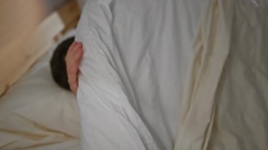 Genç bir İspanyol erkeği, rahat bir yatak odası ortamında rahatlamanın keyfini çıkarıyor. Ev ortamında rahatlık ve rahatlığı somutlaştırıyor..