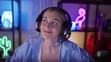 Kulaklıklı, rahat ve genç bir kadın, geceleri renkli bir oyun odasında eğleniyor..