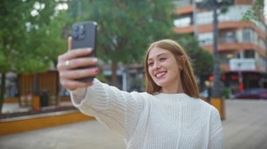 Neşeli genç bir kadın bol yeşillikli bir parkta selfie çekiyor.