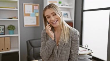 Ofiste başarılı olan sarışın iş kadını, akıllı telefondan gülümseyen ve konuşan genç kadın, büyük bir işaret veriyor, kendinden emin, pozitif ve neşeli bir yaşam tarzını kişileştiriyor.