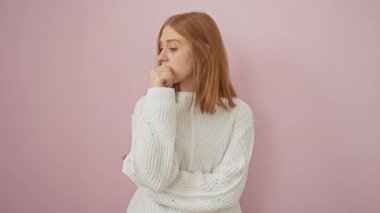 Gergin, genç, kızıl saçlı, stresli ve tırnak yiyen bir kadın, izole edilmiş pembe arka plana karşı duruyor..