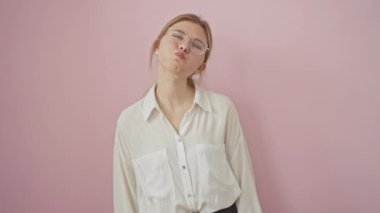 Eğlenceli genç sarışın kadın, gözlüklü, komik bir şekilde yanakları şişirirken yakalanmış, hava dolu. Pembe bir arka planda mükemmel bir şekilde izole edilmiş, komik, çılgın bir surat yapıyor.