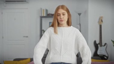 Neşeli, genç, kızıl saçlı bir kadın, kendine güveni ve neşesi tam, kolları çaprazlanmış güzel bir süveter giyiyor, rahat oturma odasındaki kameraya mutlu bir şekilde gülümsüyor. Samimi ve başarılı bir insan..